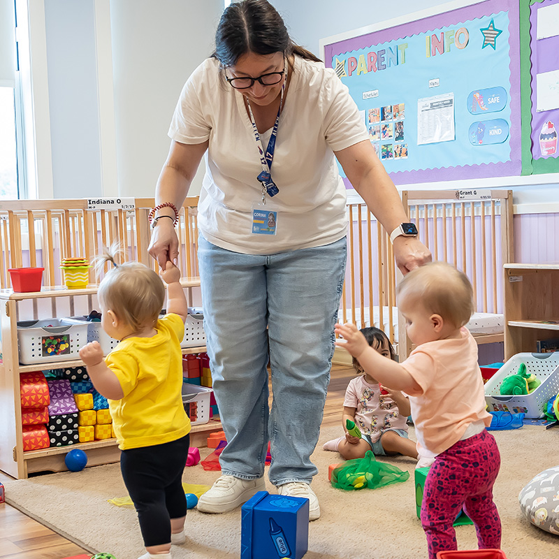 Infant teacher helping to children learning to walk